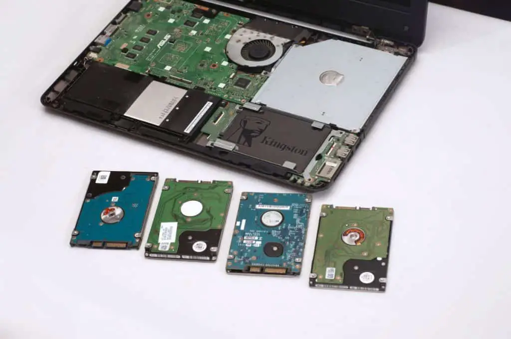 A pile of used HDD next to an open disassembled laptop or notebook computer with an SSD