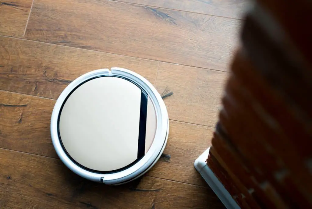 remote-controlled vacuum cleaner vacuums laminate flooring near a brick wall