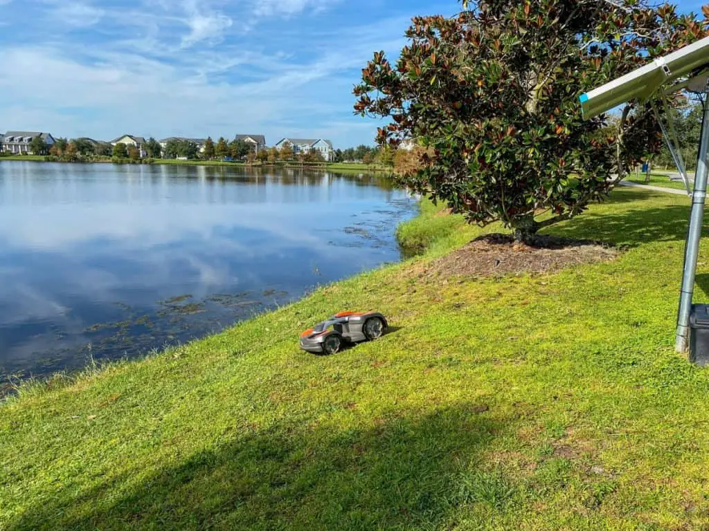 A Husqvarna autonomous lawn mower mowing near a lake